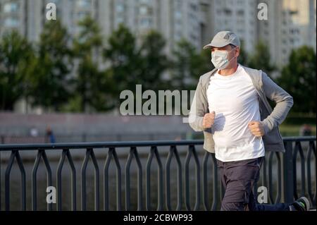 Reife kaukasischen Mann in medizinischen Gesichtsmaske Joggen in der Stadt Stockfoto