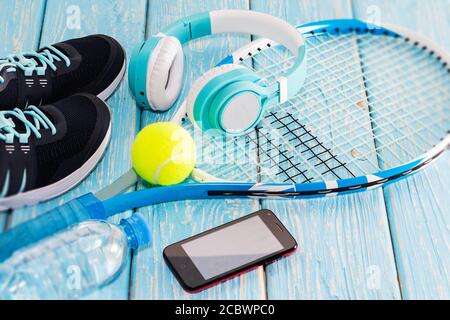 Tennisschläger. Hellblauer Hintergrund. Turnschuhe, Rakete, Ball, Wasserflasche, Musik-Kopfhörer. Stockfoto