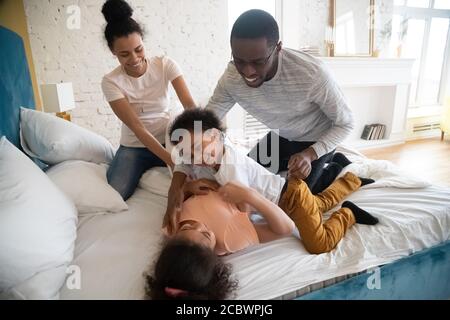 Niedliche schwarze Familie Eltern und Kinder kitzeln auf dem Bett Stockfoto