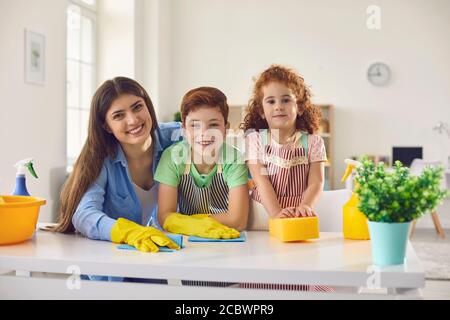 Glückliche Familie mit Mutter und zwei Kindern, die zu Hause aufräumen. Eltern und Kinder tun Hausarbeiten zusammen drinnen Stockfoto