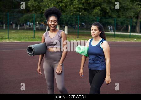 Schöne Freundinnen stehen mit Sportteppichen auf der Straße und machen sich bereit für den Sport. Stockfoto