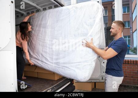 Paar Entladen Matratze Aus Van Oder Lkw Während Umzug Haus Im Freien Stockfoto