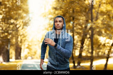 Schöner schwarzer Sportler im Hoodie, der am Herbsttag im Freien läuft Stockfoto
