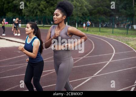 Eine schwarze und kaukasische Frau joggt auf der Straße in einem spezialisierten Ort. Sport - ist das Leben. Stockfoto