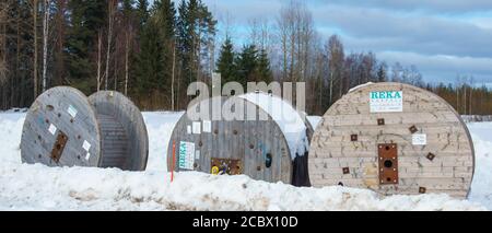 Große hölzerne Kabelrollen, die draußen auf Schnee im Winter in Finnland liegen Stockfoto