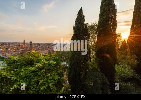 Blick durch Zypressen am Castel San Pietro Blick auf den Sonnenuntergang mit Sonnensternen über der Altstadt von Verona, Italien Stockfoto