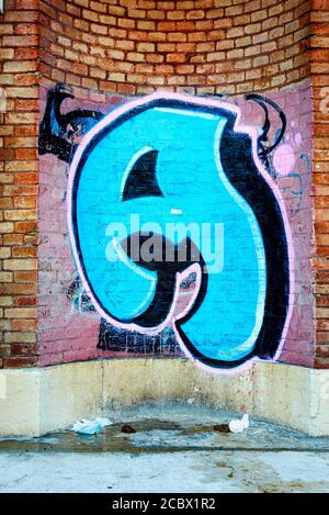 Blaue Graffiti von Charakter A auf Terrakotta-Mauer und Müll und Dolden auf dem Boden, Verona, Italien Stockfoto