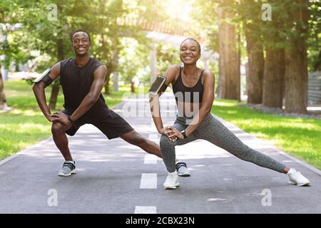 Black Runner Paar Stretching Muskeln Im Freien, Aufwärmen Vor Dem Joggen Im Park Stockfoto
