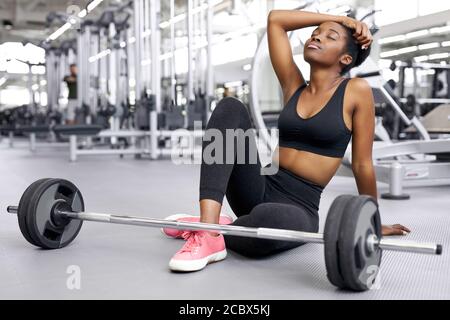 crossfit afrikanische Frau sitzt im Fitnessstudio, Ruhe, eine Pause nach dem Cross-Fit-Training mit Langhantel. Kraft, Kraft, gesunder Lebensstil, Sportkonzept Stockfoto