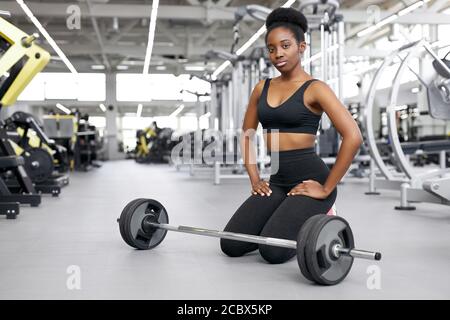 crossfit afrikanische Frau sitzt im Fitnessstudio, Ruhe, eine Pause nach dem Cross-Fit-Training mit Langhantel. Kraft, Kraft, gesunder Lebensstil, Sportkonzept Stockfoto