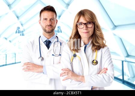 Aufnahme von weiblichen und männlichen Ärzten, die auf einem isolierten weißen Hintergrund zusammen stehen, während sie die Kamera betrachten und lächeln. Medizinisches Team. Stockfoto