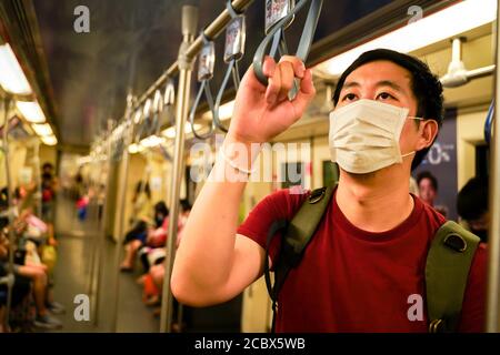 Junger erwachsener asiatischer Mann mit Gesichtsmaske im U-Bahn-Zug in Bangkok, Thailand. Neuer normaler Lebensstil während Covid19 - Coronavirus Pandemie Stockfoto