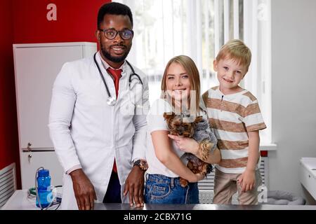 Porträt von lächelnden Hundebesitzer und afrikanischen Tierarzt Arzt in der Klinik, sie schauen auf Kamera nach der medizinischen Untersuchung Stockfoto