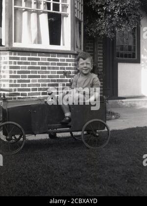 Um die 1940er Jahre, historischer, zwitschernder kleiner Junge, der in seinem Metall-Pedalauto sitzt, handgefertigt, mit Kastenkonstruktion, Drahträdern und kleiner Tür, England, Großbritannien. Stockfoto