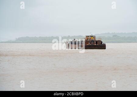 Ein rostiger alter Lastkahn, der Eisenerz oder Kohle transportiert und den Zuari Fluss in Goa, Indien, kreuzt Stockfoto