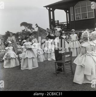 1950er Jahre, historisch, ein kleiner Junge in einem Regentenkostüm mit Spitzenkräften, der Trompete spielt, um die Krönung der „Rose Queen“ in Farnworth, Bolton, Lancashire, England, Großbritannien anzukündigen. Eines der Mädchen hält ein Kissen mit der zeremoniellen Krone. Seit den 1880er Jahren findet das jährliche Rose Queen Festival traditionell im Juni statt und wurde nach den Kriegen der Rosen (1455–87) zu einem jährlichen Event in vielen Städten und Dörfern in ganz Großbritannien, insbesondere im County Lancashire, bekannt als Red Rose County. Stockfoto