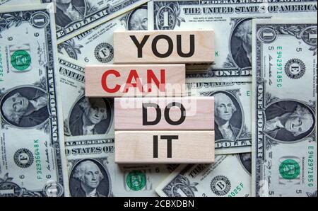 Konzept für die Schaffung einer Erfolgsgrundlage. Holzblöcke mit dem Text 'Du kannst es tun'. Schöner Hintergrund von Dollarscheinen. Stockfoto