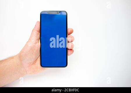 Eine Person, die ein Smartphone mit einem blauen Bildschirm auf weißem Hintergrund hält. Stockfoto