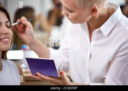 Prozess der Herstellung Make-up in Schönheitssalon. Visagiste arbeiten mit Pinsel auf Modell Gesicht. Anwendung Ton auf die Haut. Professionelle Make-up Künstler malt Modell Stockfoto