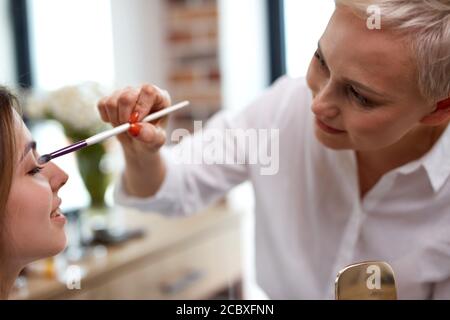 Prozess der Herstellung Make-up in Schönheitssalon. Visagiste arbeiten mit Pinsel auf Modell Gesicht. Anwendung Ton auf die Haut. Professionelle Make-up Künstler malt Modell Stockfoto