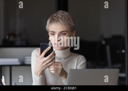 Glückliche junge kurzhaarige blonde Geschäftsfrau Blick auf Smartphone-Bildschirm. Stockfoto