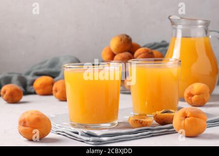 Aprikosensaft mit Fruchtfleisch in zwei Gläsern und einer Kanne auf grauem Hintergrund, Closeup Stockfoto