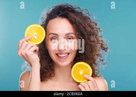 Fröhliche Frau mit dunklen langen welligen Haaren, die zwei Scheiben halten Von frischer saftiger Orange Stockfoto