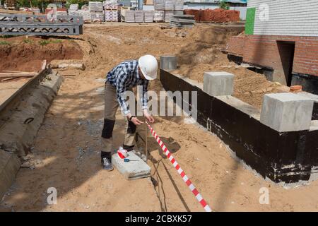 Der Aufseher auf der Baustelle bindet das Signalband für die Einzäunung des Territoriums an. Zaun des sicheren Bereichs auf der Baustelle. Konstr Stockfoto