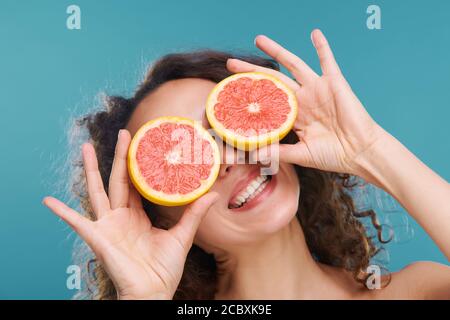 Junge fröhliche Frau hält Scheiben von frischen saftigen Grapefruit durch Ihre Augen Stockfoto
