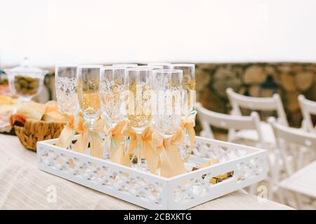 Hochzeitsglas mit Muster und beigen Schleifen auf einem durchbrochenen weißen Tablett auf dem Tisch. Stockfoto