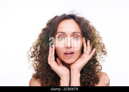 Wunderschöne junge Frau mit langen braunen welligen Haaren halten Hände An ihrem Gesicht Stockfoto