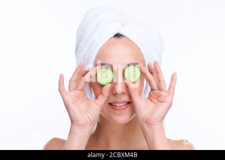 Junge glückliche Frau mit weißem Handtuch auf dem Kopf halten Scheiben Frische Gurke Stockfoto