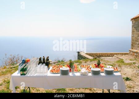 Ein festlich serviertes Buffet mit Wasser, Champagner und Früchten auf Tellern vor dem Hintergrund eines alten Gebäudes am Wasser. Stockfoto