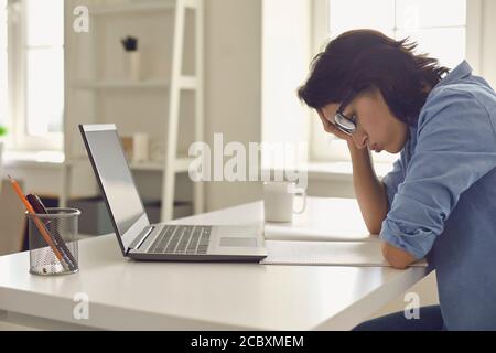 Erschöpfte junge Frau, die vor dem Laptop im Heimbüro an schwierigen Aufgaben arbeitet. Freiberufler fühlen sich am Arbeitsplatz müde Stockfoto