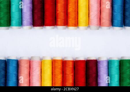 Farbe Nähfäden auf weißem Hintergrund, Draufsicht. Nähproduktion. Reihen von Spulen des Gewindes in verschiedenen Farben. Bunte Garnrollen in der Textilindustrie. Banneridee. Fadenstruktur. Stockfoto