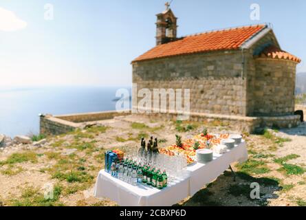 Festlich serviertes Buffet mit Wasser, Champagner und Früchten auf Tellern vor dem Hintergrund einer alten Backsteinkirche. Stockfoto