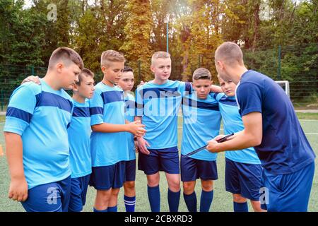 Kinder in Fußball-Uniform umarmt und hört zu erklären Trainer. Stockfoto