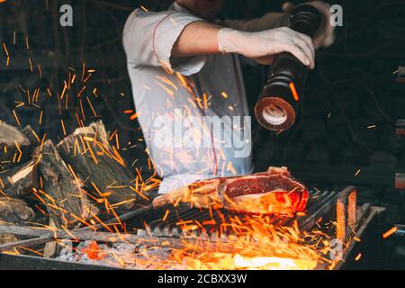 Kochen Steak in einem Steinofen. Der Koch pfeffert das Steak auf dem Feuer. Stockfoto