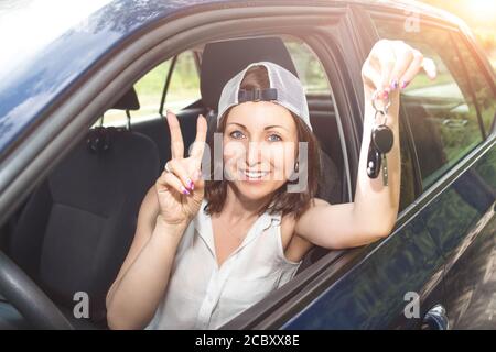 Schöne Frau in einem Hut hält Schlüssel zu neuen gekauften Auto und lächelt an der Kamera im Sommer sonnigen Tag. Frau fährt ein Auto Stockfoto