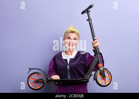 Glamouröse fröhliche Frau hält einen Roller in den Händen, Oma hat Geschenk für ihre Enkeltochter gekauft, Enkel am Geburtstag. Nahaufnahme Porträt. Stockfoto