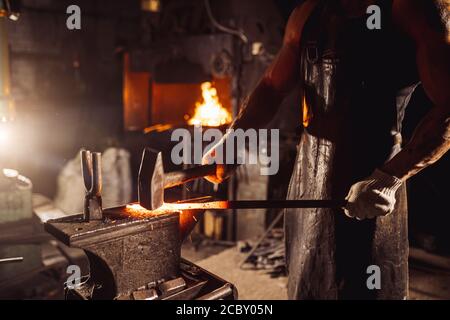 Junger bärtiger Mann in Lederuniform heizt das Metall an Brandisolierarbeiten in der Werkstatt Stockfoto