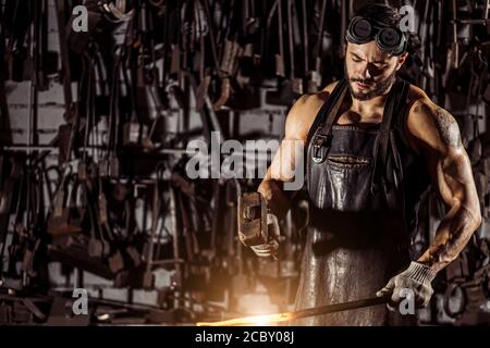 Junger muskulöser Schmied Mann manuell Schmieden der geschmolzenen Metall. Schmied hämmert heiße Metall-Pfeilklinge, trägt Lederschürze Stockfoto