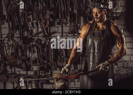 Junger muskulöser Schmied Mann manuell Schmieden der geschmolzenen Metall. Schmied hämmert heiße Metall-Pfeilklinge, trägt Lederschürze Stockfoto