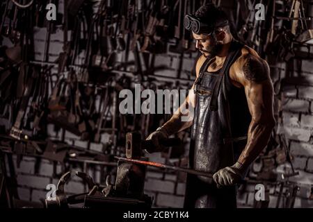 Junger muskulöser Schmied Mann manuell Schmieden der geschmolzenen Metall. Schmied hämmert heiße Metall-Pfeilklinge, trägt Lederschürze Stockfoto