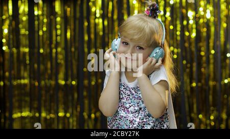 Kind tanzt, hört Musik über Kopfhörer. Energetisch im Rhythmus bewegen, entspannen, genießen, hun. Wenig Spaß blonde Kind Teenager-Mädchen 5 Jahre alt isoliert auf golden glänzenden Hintergrund im Studio Stockfoto