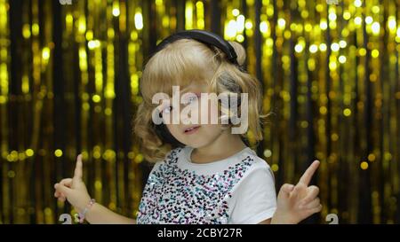 Kind tanzt, singt, hört Musik über Kopfhörer. Energetisch im Rhythmus bewegen, entspannen, genießen, hun. Wenig Spaß blonde Kind Teenager-Mädchen 5 Jahre alt isoliert auf glänzendem Hintergrund im Studio Stockfoto