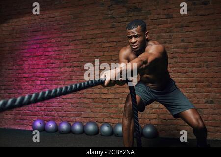 African Cross fit Trainer steht mit Kampfseilen beweist, dass dynamisches Training mit Seilen Stärkung des Sportlers Körper. Stockfoto