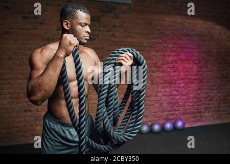 African Cross fit Trainer steht mit Kampfseilen beweist, dass dynamisches Training mit Seilen Stärkung des Sportlers Körper. Stockfoto