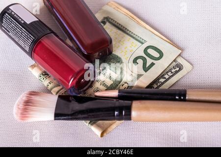 Ein flaches Lay Foto von roten Lippenstiften und Make-up Bürsten alle auf gefalteten Dollar Scheine Stockfoto