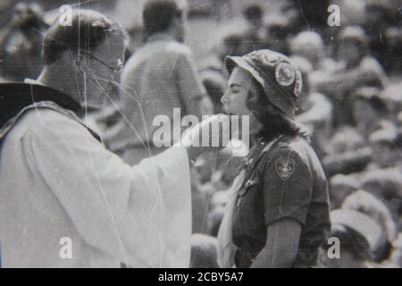Feine 70er Jahre Vintage Schwarz-Weiß-Fotografie eines Priesters, der die heilige Kommunion bei einer Outdoor-Scouting-Veranstaltung gibt. Stockfoto